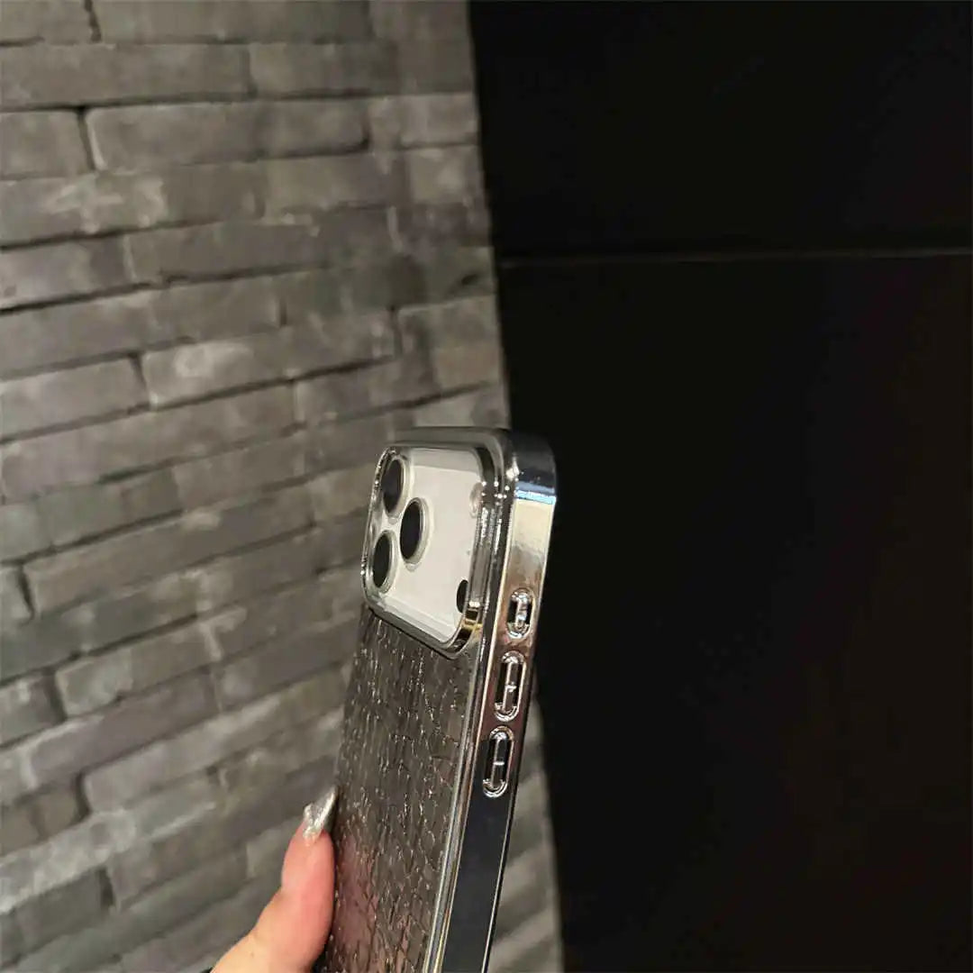 A close-up of a hand holding a smartphone with a clear, metallic, and textured protective case against a gray brick wall and black background.