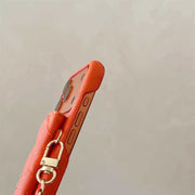 Close-up of a red leather phone case with a gold ring on a beige background