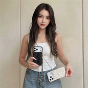 Woman holding a phone with a black case and a white quilted handbag against a plain background