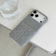Gray phone case with quilted design on a white surface next to a glass of water.