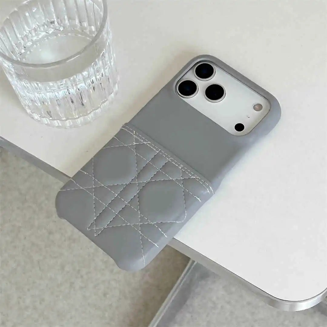Gray phone case with quilted design on a white surface next to a glass of water.