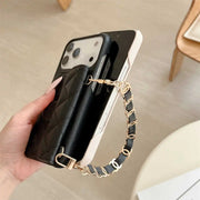 Hand holding a black phone case with a gold chain strap on a light background