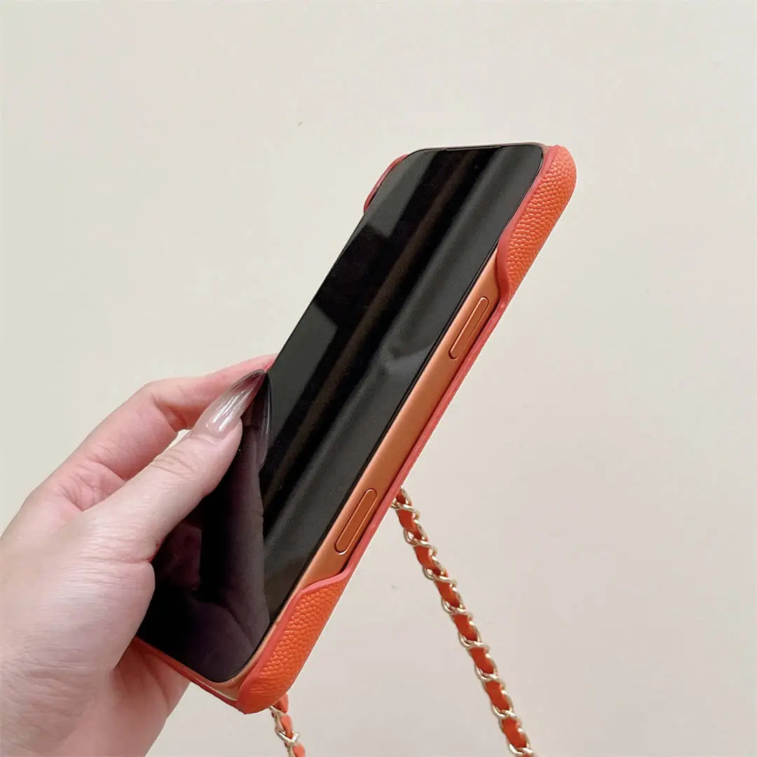 Hand holding an orange phone case with a chain strap against a light background