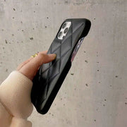 Person holding a black quilted phone case against a concrete wall.